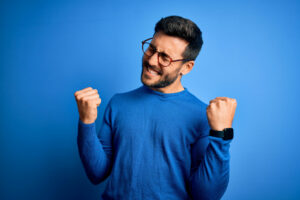junger-mann-im-blauen-pulli-macht-jubelnde-geste-vor-blauen-hintergrund