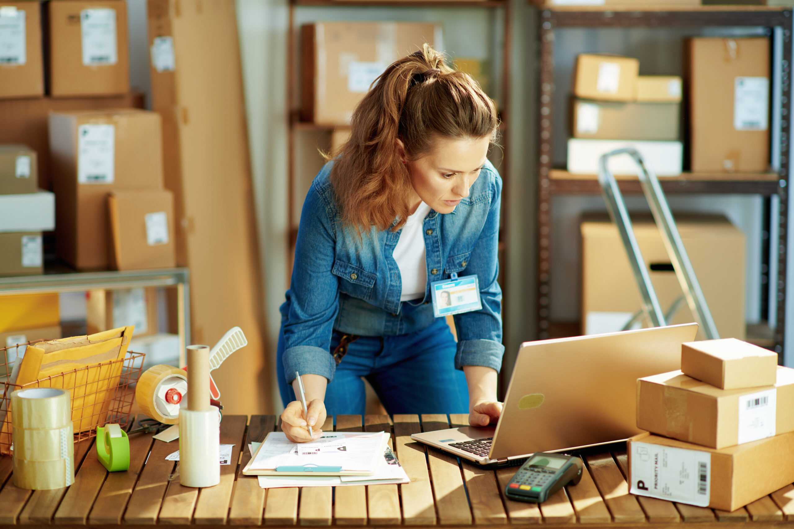 junge-frau-im-lagerhaus-mit-laptop-macht-sich-notizen